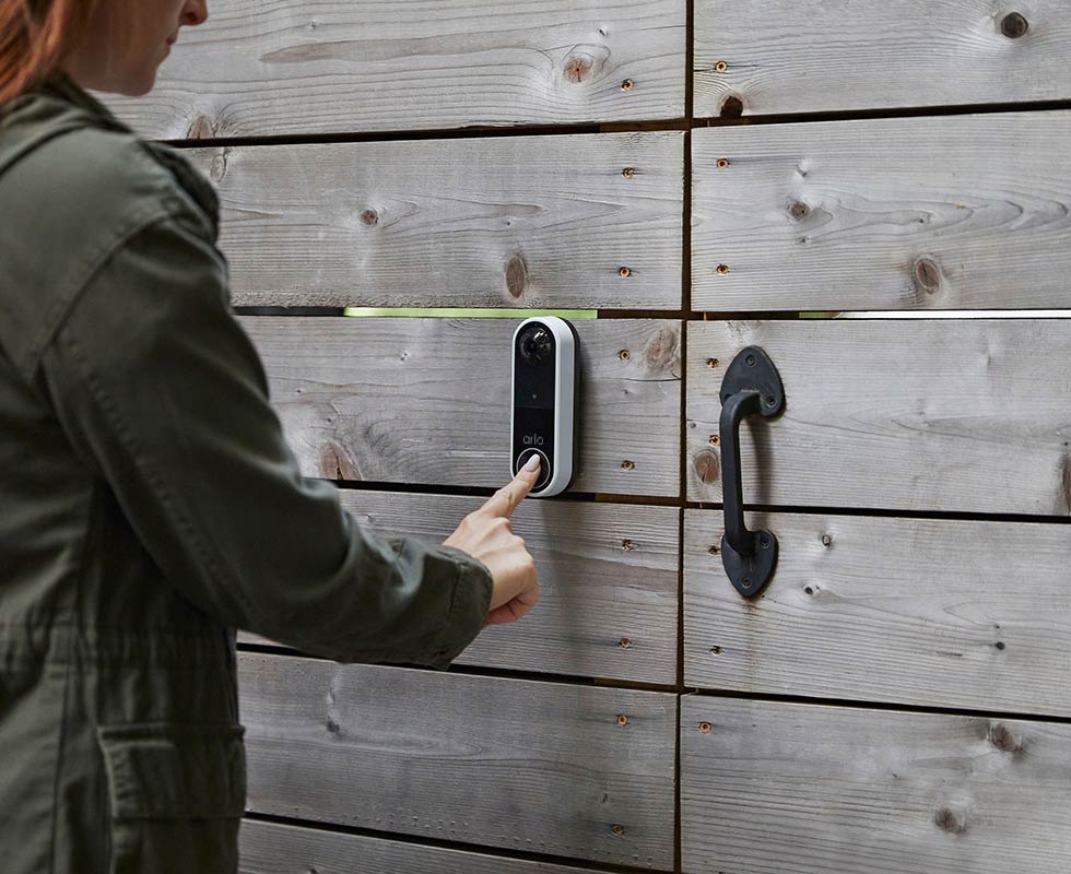 Person ringing Arlo wireless video doorbell at entrance to backyard