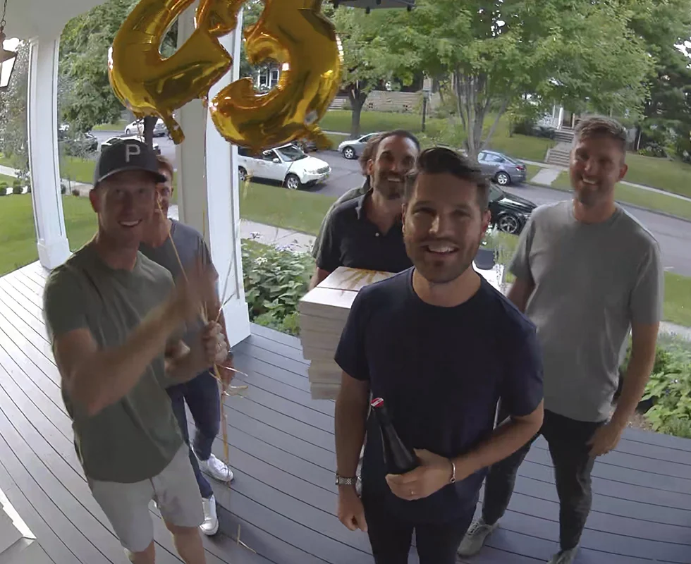footage from the Arlo pro 4 security camera of a group of guests carrying balloons and gifts at the front entrance to a house