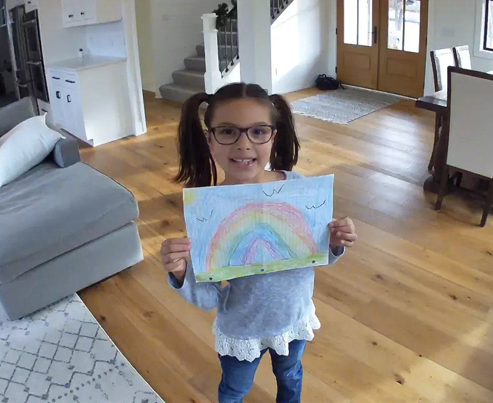 Child holding up a drawing to the Arlo Essential Indoor security camera