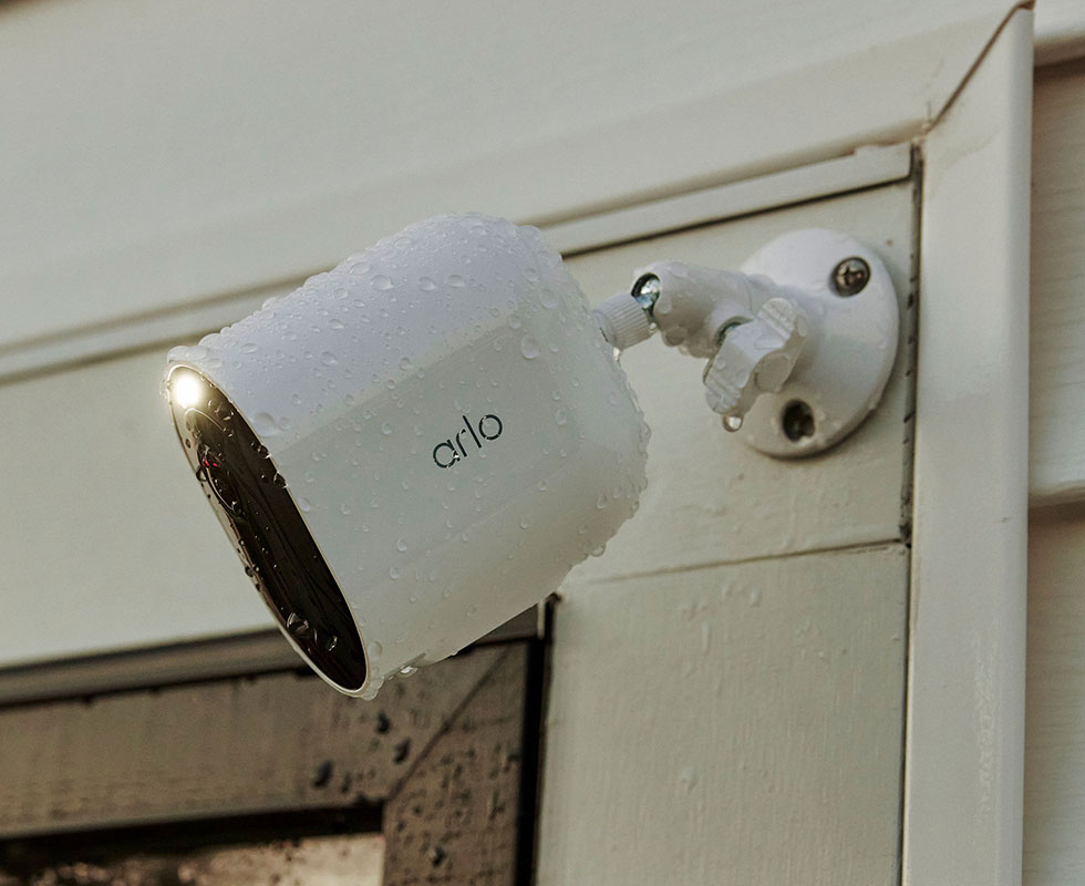 Arlo Ultra 2 wireless security camera positioned and mounted onto the side of a house during rainy weather