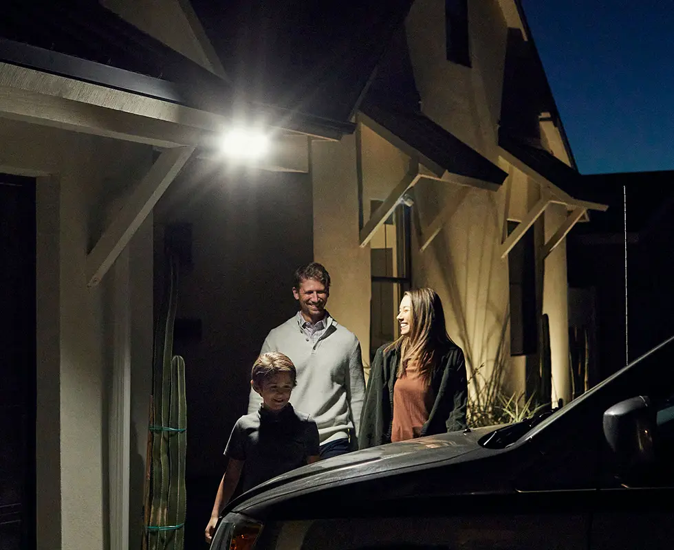 Arlo Pro 3 wireless floodlight camera illuminating a driveway with a family and car in view at night