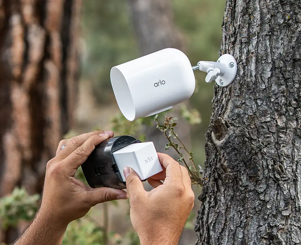 Arlo Go 2 wireless security camera attached to a tree with hands replacing the battery