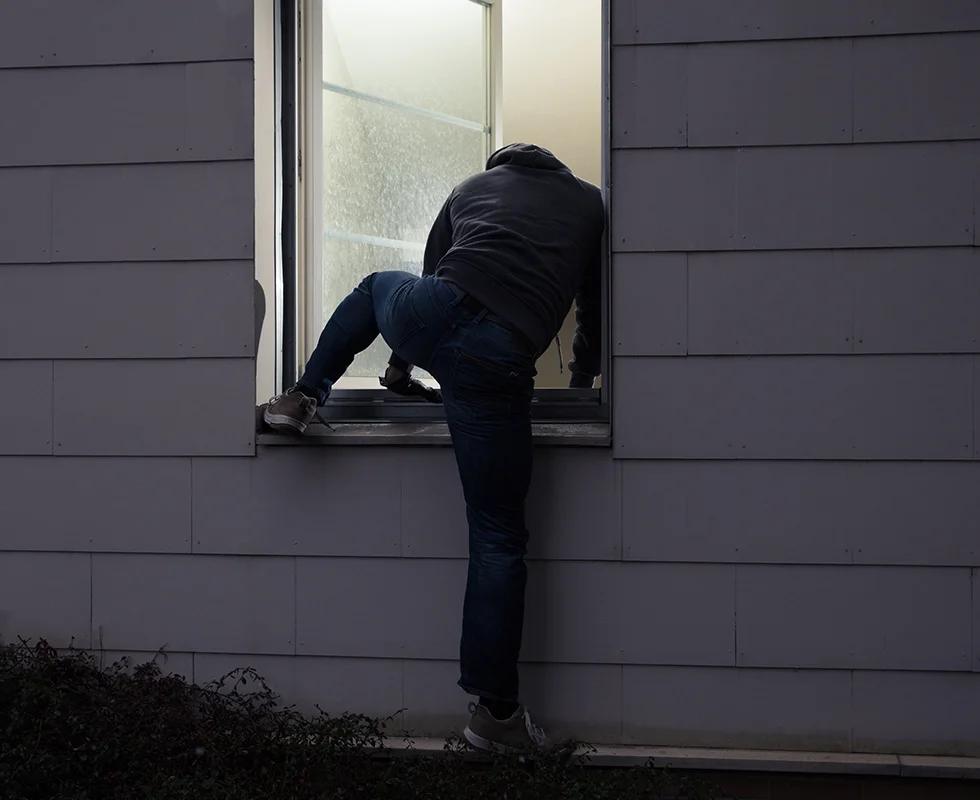 Burglar sneaking into a house through an open window